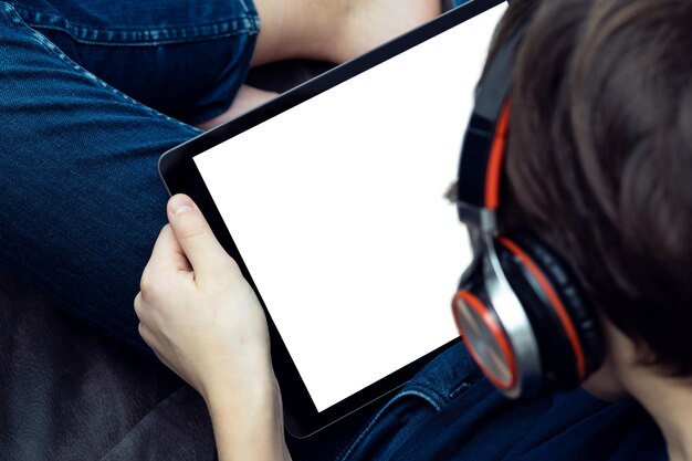 Digital tablet computer with blank white screen in male hands from above view closeup Young guy in headphones