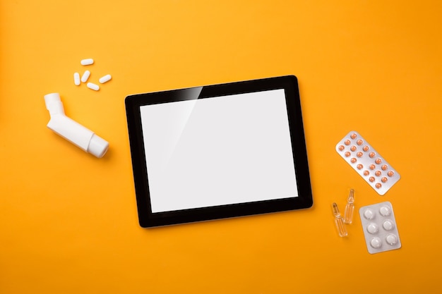 Digital tablet in doctors desk with inhaler and pills. Top view with place for your text.