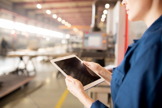 Digital tablet in hands of young professional technician surfing in the net for online data while serving industrial machines