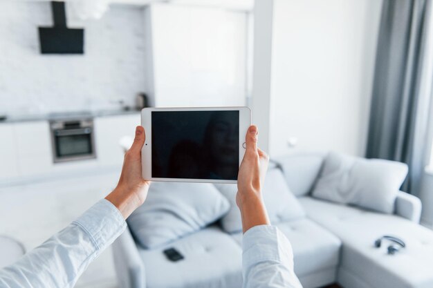 手にデジタルタブレット若い女性は日中にスマートハウスの部屋で屋内にいます