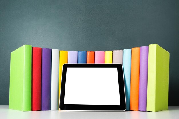 Digital tablet on table with colored books on background