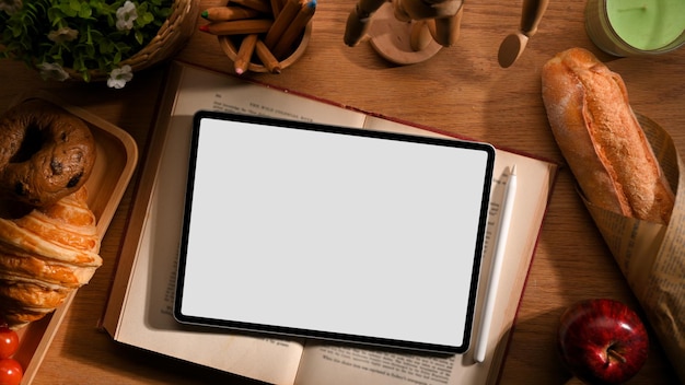 Un mockup di schermo vuoto touch tablet digitale su un libro di ricette con prodotti da forno sul tavolo in legno vista dall'alto