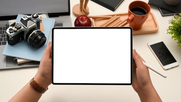 A digital tablet touchpad white screen mockup in a woman hands over office desk background