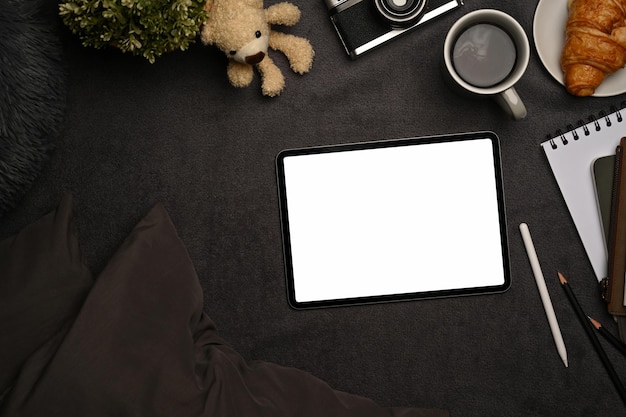 Digital tablet with blank screen, coffee cup and camera on gray carpet.