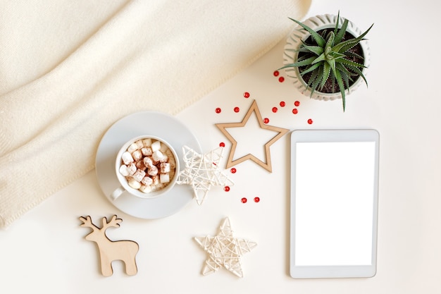 A digital tablet with a blank screen lies on a white table surrounded by flat wooden Christmas