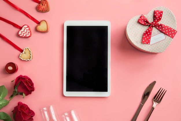 Digital tablet with blank screen, roses, hearts and gift box. top view.