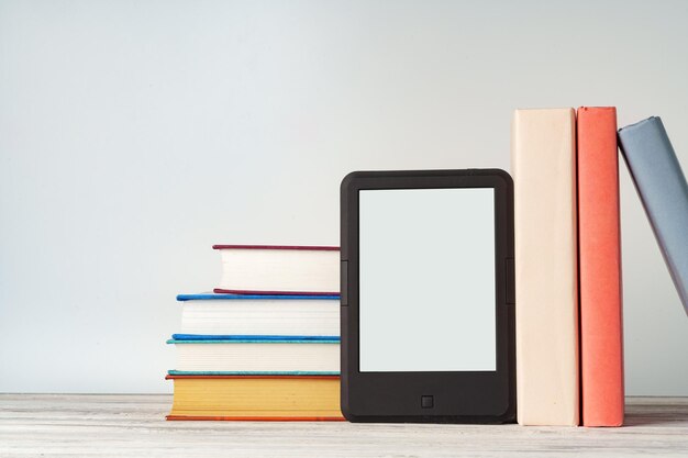 Digital tablet with a stack of books on gray background