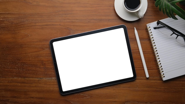 Digital tablet with white screen coffee cup glasses and notepad on wooden office desk