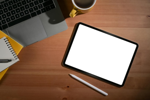 白い画面のラップトップコーヒーカップと木製のオフィスデスクのノートブックフラットレイとデジタルタブレット