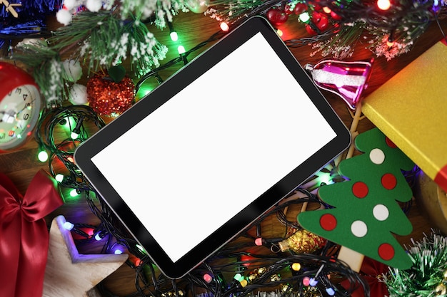 クリスマスの見掛け倒しと花輪のクローズアップの間に横たわる白い画面とデジタルタブレット。クリスマスプレゼントのコンセプト