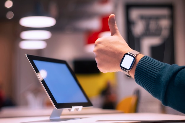 Digital tablet with white screen on the table and smart watch on man's hand doing ok sign