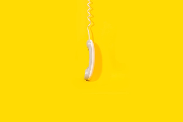 A digital telephone receiver hanging down on a yellow background with copy space