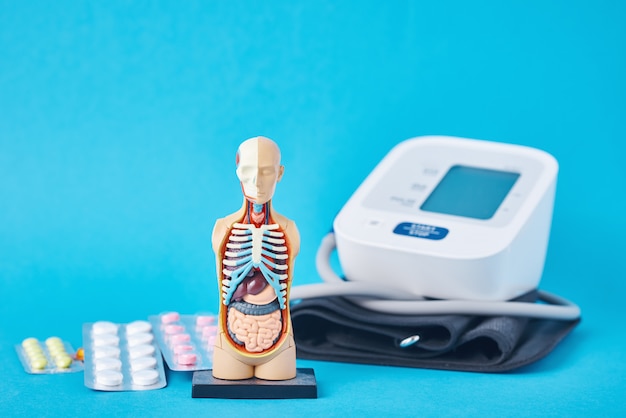 Digitale bloeddrukmeter, anatomische dummy man etalagepop en medische pillen op blauwe achtergrond. Gezondheidszorg en geneeskunde concept