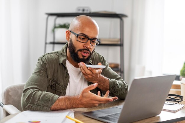 Digitale luidsprekertoepassing Latijnse zakenman met stemassistent op mobiele telefoon die op laptop thuis werkt