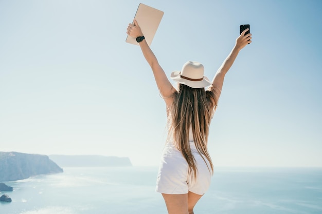 Digitale nomade vrouw in de hoed een zakenvrouw met een laptop zit op de rotsen bij de zee tijdens