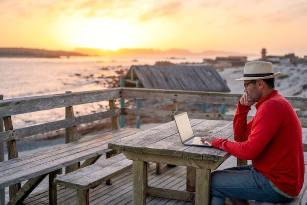 Digitale nomade zit buiten op het strand met een laptop die alleen telewerk doet bij zonsondergang