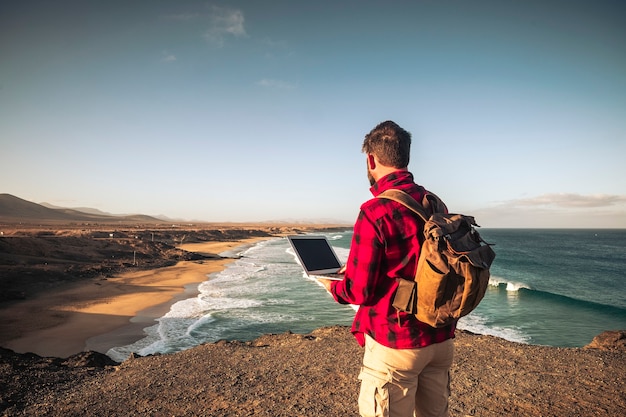 Digitale nomaden mensen slim werken concept met staande man werken met laptopcomputer en internetverbinding roaming in wilde buitenplaats met geweldig uitzicht op het strand