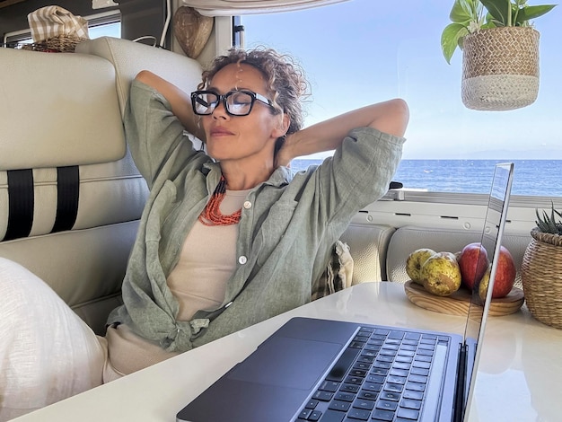 Foto digitale nomadische reiziger die zich ontspant in een moderne camper van met de oceaan op de achtergrond buiten het raam laptop op de tafel afstandswerker vrijheid concept levensstijl vrouw