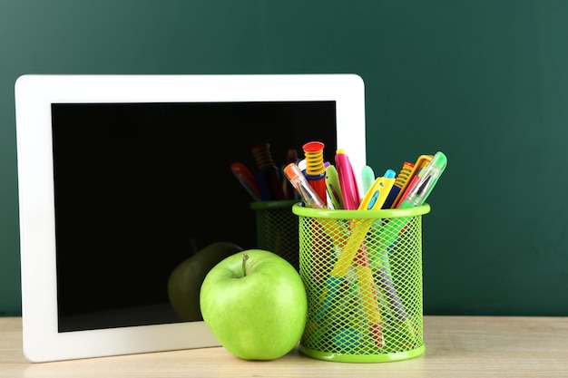 Digitale tablet kleurrijke pennen en appel op bureau voor bord