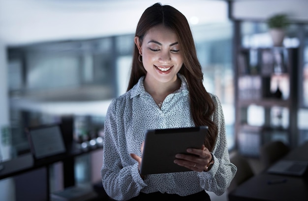 Photo digitising her way to the deadline shot of a young businesswoman using a digital tablet in an office at night