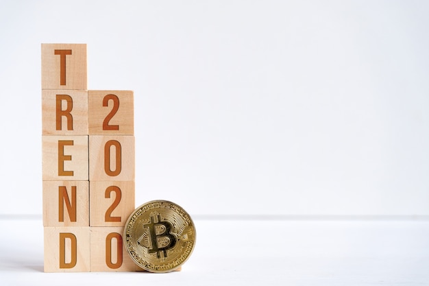 Digits 2020 and the word trend on wooden cubes on a white background next to a bitcoin coin.