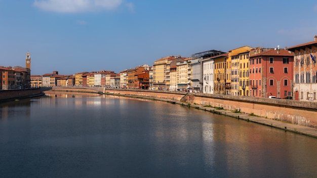 Dijk met oude stadsbrug en gebouwen en reflecties in stilstaand water op een zonnige dag Pisa Italië