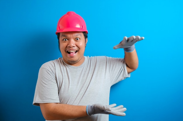 Dikke Aziatische man met een helm presenteert iets in zijn hand terwijl hij zijwaarts kijkt. de man toonde een uitdrukking van vreugde en verbazing