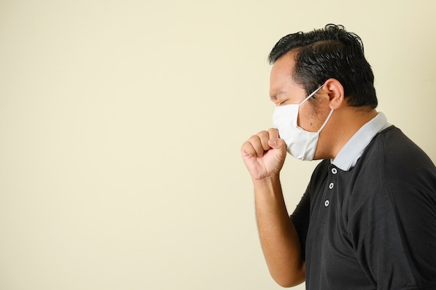 Dikke Aziatische man met een masker hoest terwijl hij zijn mond sluit met zijn handen, hij voelt zich onwel. symptomen van corona virusziekte