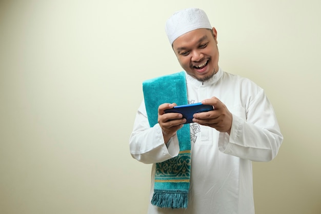 Dikke Aziatische moslimman ziet er zelfverzekerd uit terwijl hij zijn smartphone gebruikt