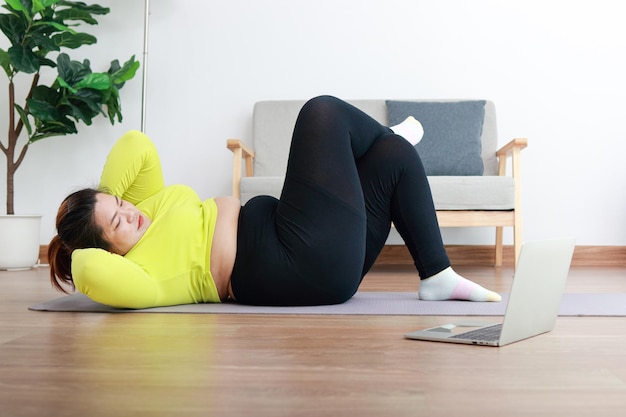 Foto dikke aziatische vrouwen trainen om af te vallen liggend op de houten vloer in huis voer oefeningen uit door online video fitnesstrainers te volgen op uw laptop computer sportconcept gezonde oefening