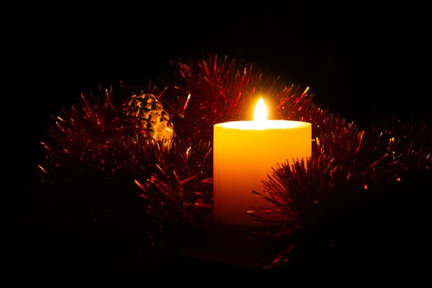 dikke brandende kaars staat omringd door rood kerstklatergoud In de buurt staat een nieuwjaarsglas om