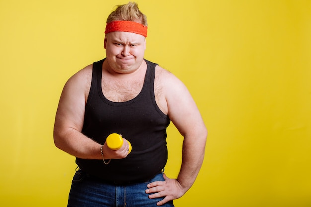 Dikke man probeert kleine gele dumbell op te tillen