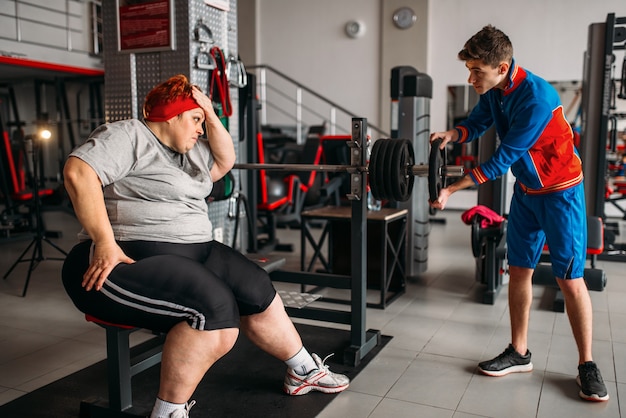 Dikke vrouw met behulp van barbell, training met instructeur