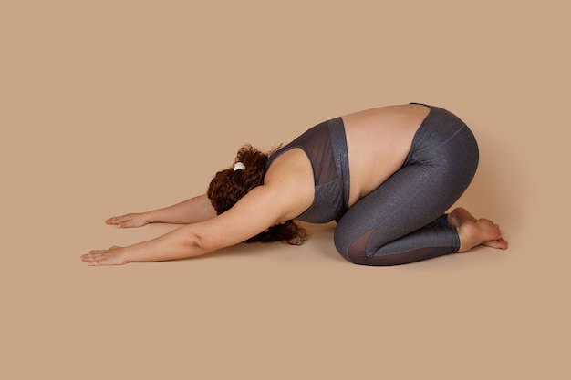 Dikke vrouw met overgewicht met massieve schouders in grijs sportuniform klaar voor gymnastiek Pilates yoga Foetale positie