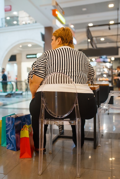 Dikke vrouw zit aan de tafel in fastfoodrestaurant, achteraanzicht. Overgewicht vrouwelijke persoon in winkelcentrum fastfood, obesitasprobleem