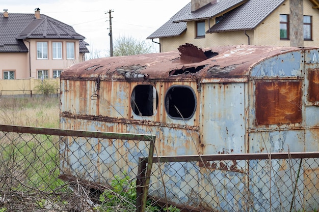 作業現場の老朽化した腐った錆びた金属製の小屋丸い屋根と、トレーラードローバーのある牧草地または牧草地からの壊れた窓のある古いブリキの建設用トレーラー