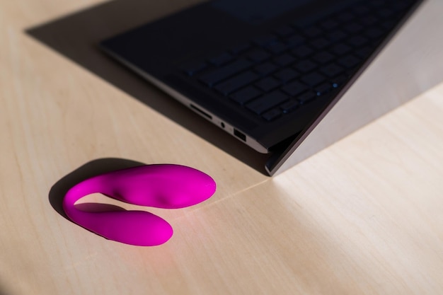 Dildo op tafel naast een laptop Het concept van online seks Gebogen roze vibrator voor vrouwelijke zelfgenoegzaamheid Stimulator voor de clitoris