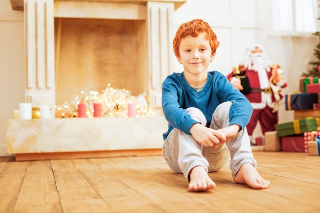 勤勉な子供。自宅で陽気な笑顔で木の床でリラックスしている生姜の少年のローアングルショット。