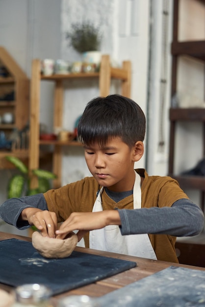 テーブルで粘土のボウルやマグカップを作る勤勉な男子生徒