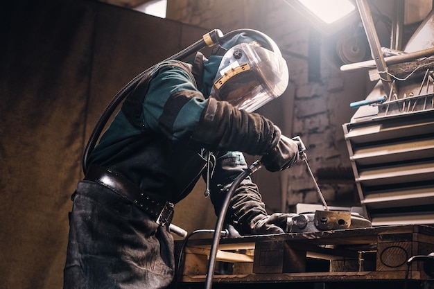 Diligent worker in protective mask making welding while working at his workplace.