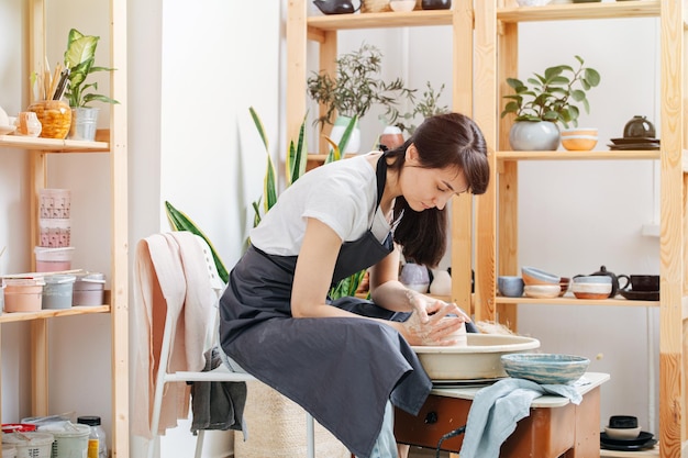 ワークショップでろくろで粘土を形作る勤勉な若い女性