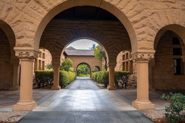 Diminishing perspective of empty footpath amidst plants with arched built structure at Stanford University in Palo Alto at California