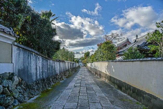 Diminishing perspective of footpath against cloudy sky