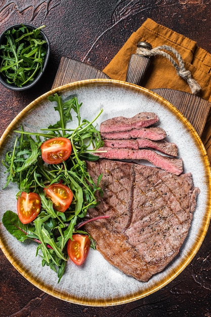 Diner met gegrilde kalfsvlees steaks en groentesalade. Donkere achtergrond. Bovenaanzicht.