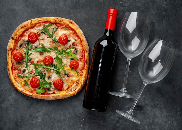 Diner voor twee. heerlijke italiaanse pizza met mozzarella kaas, champignons, tomaat, paprika, ui en een fles wijn met glazen.