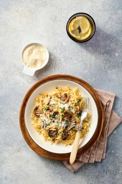 Dining italian pasta risoni with mushrooms and parmesan cheese on concrete surface. Top view