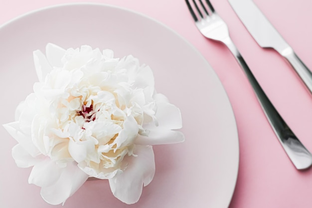 이벤트 장식 및 디저트 메뉴를 위한 분홍색 배경 상단 식기에 웨딩 장식으로 모란 꽃을 곁들인 식탁과 칼붙이