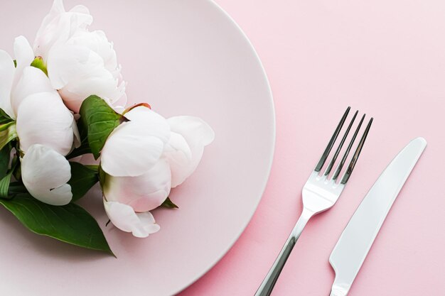 Обеденная тарелка и столовые приборы с цветами пиона в качестве свадебного декора на розовом фоне верхняя посуда для украшения мероприятия и брендинга меню