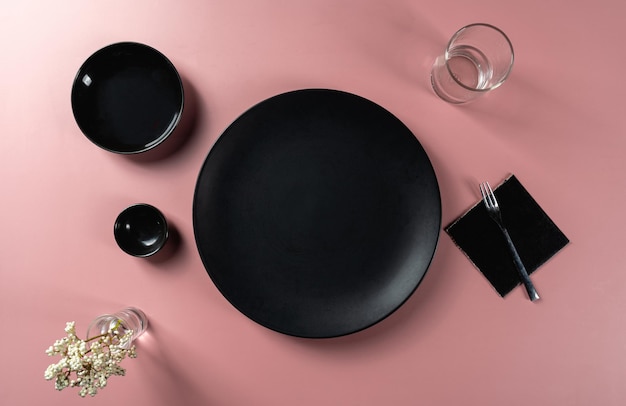 Dining set up with empty black plate set placed on pink background