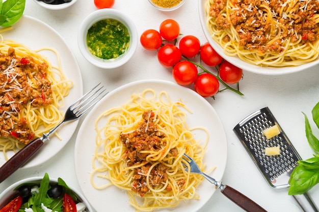 ダイニングテーブルのコンセプト。ボロネーゼソースのスパゲッティ、野菜と野菜のサラダ、オリーブ、パルメザンチーズとスパイス